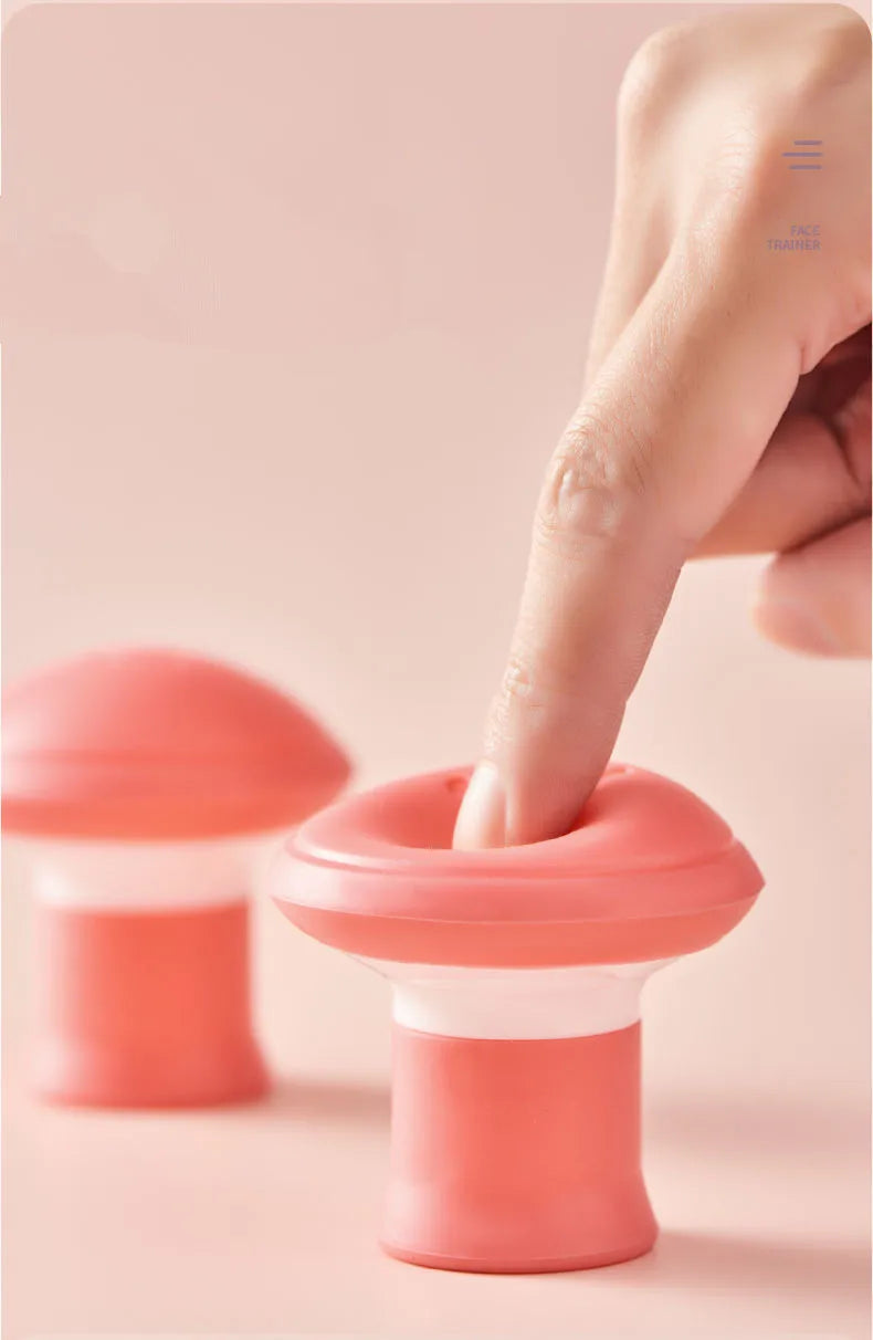 A finger presses into a mushroom-shaped, pink and white silicone facial exerciser on a light pink background.