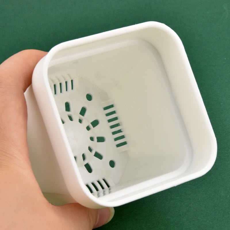 White square flower pot base showing drainage holes, close-up held by hand