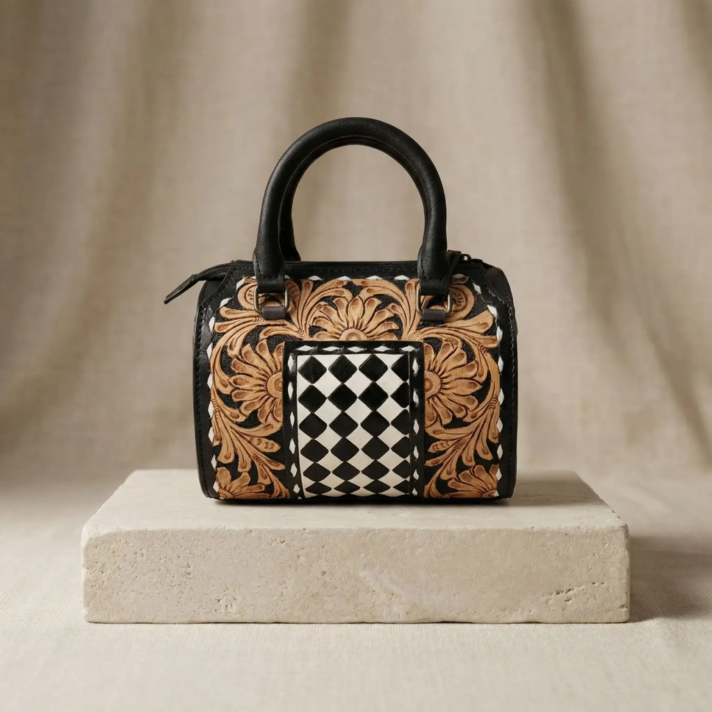 Hand-tooled leather trunk bag with floral carving, black and white checkered panel, and black leather handles.