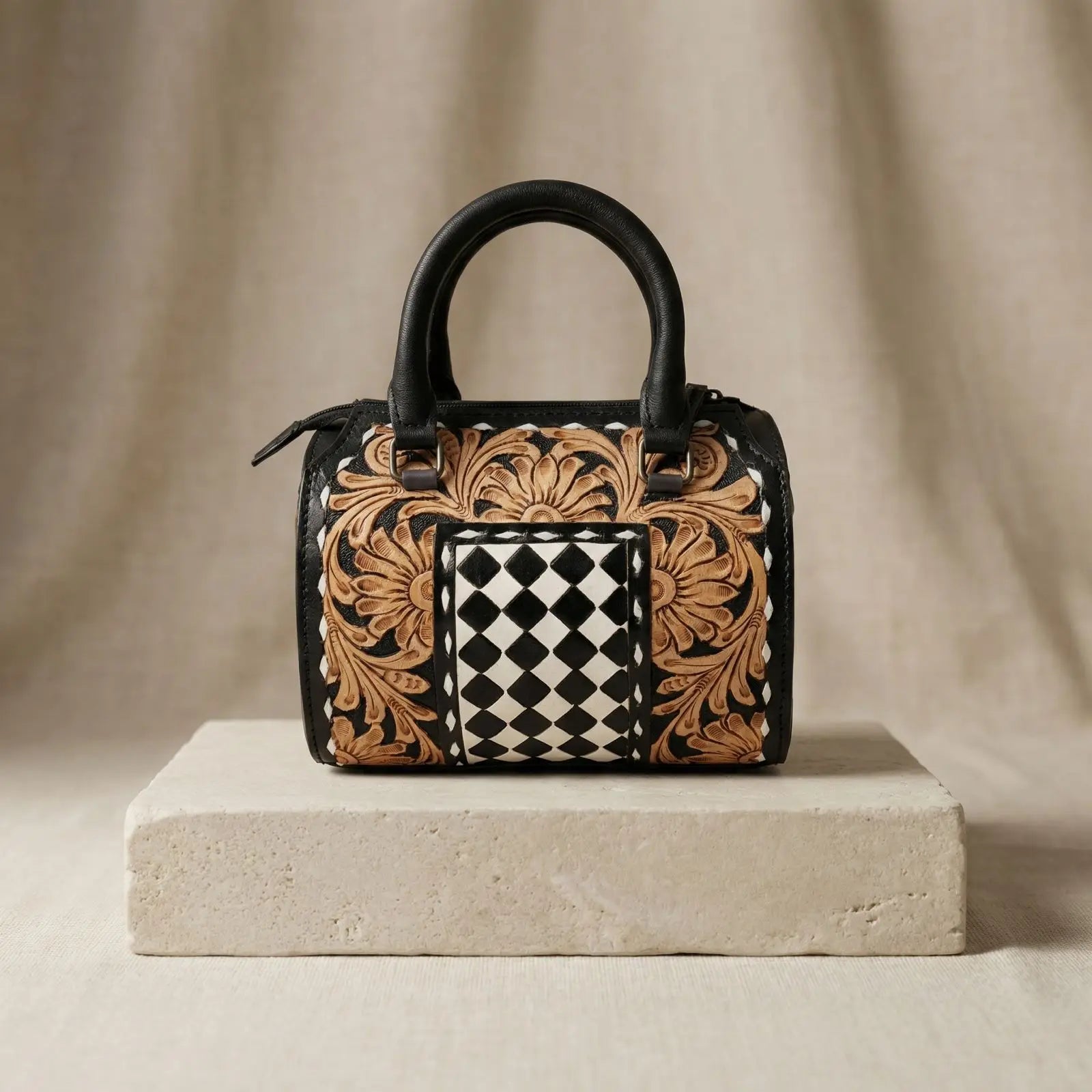 Hand-tooled leather trunk bag with floral carving, black and white checkered panel, and black leather handles.