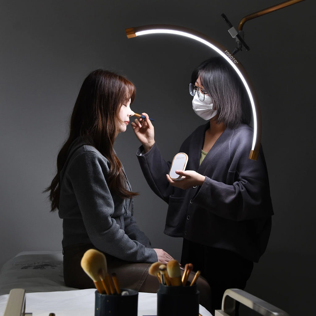 Curved LED beauty lamp providing bright, focused lighting for a makeup artist applying cosmetics to a client.