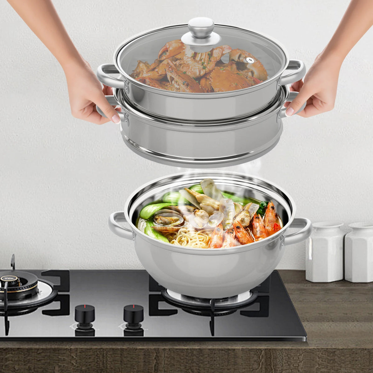 Three-tier stainless steel steamer pot with domed lid on stovetop, hands gripping handles.