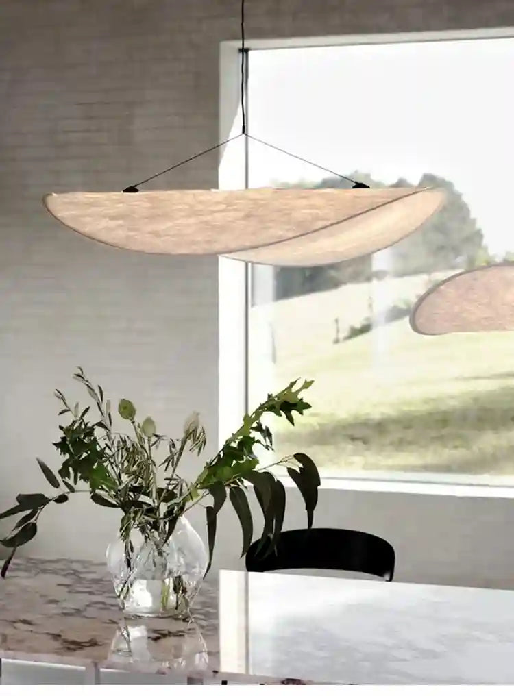 Large, curved, beige pendant lamp made of textured fabric, suspended by thin wires above a dining room table.