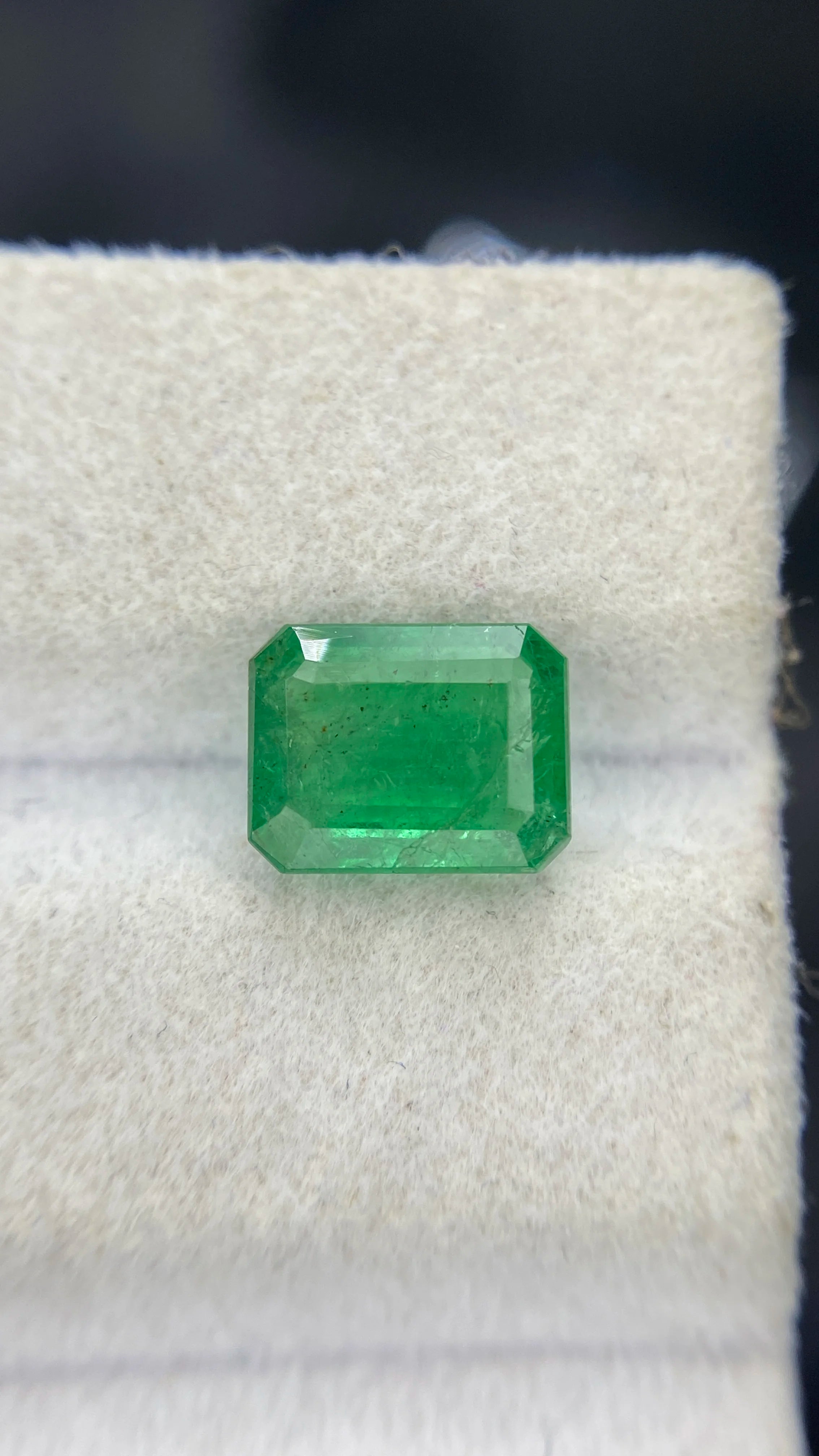 Green octagon emerald-cut loose gemstone centered on white felt
