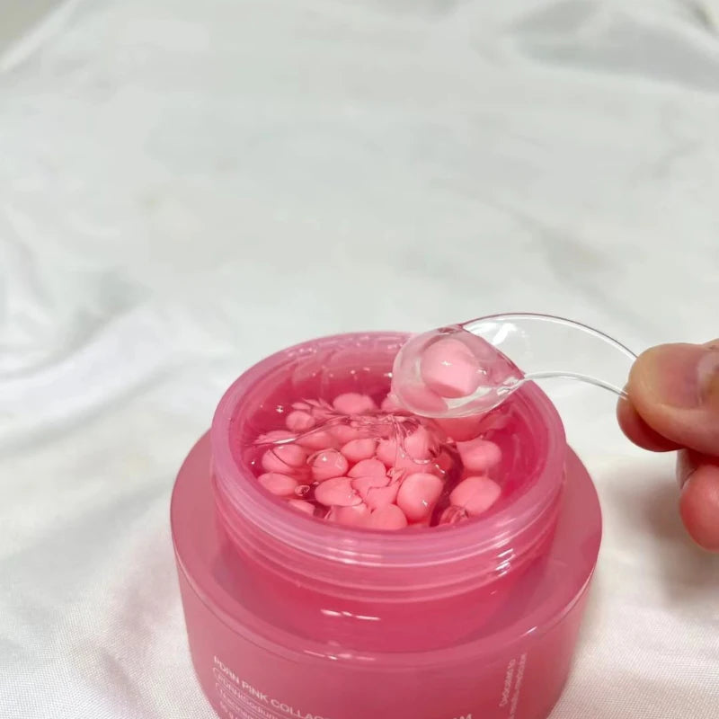 Pink jar of collagen cream containing small pink capsules suspended in a clear, lightweight gel, scooped by a spatula.