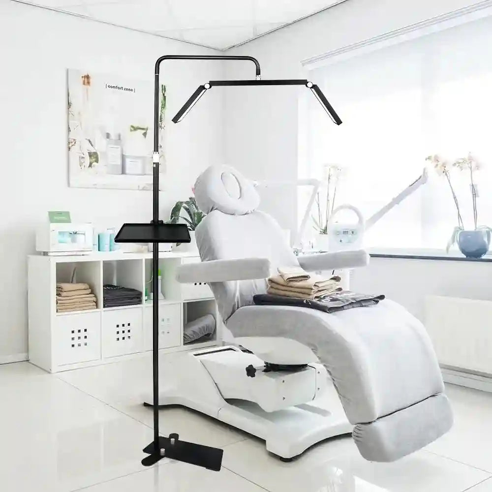 Black metal floor lamp with adjustable LED arms and a utility tray, used for beauty and spa treatment lighting.