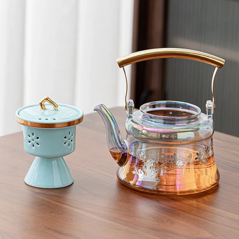 Iridescent glass teapot with gold handle and floral ceramic tea infuser set on a wooden table.