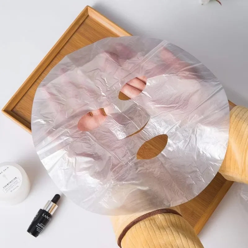 Hands hold a circular, transparent, crinkled plastic film face mask with cutouts for eyes, nose, and mouth.