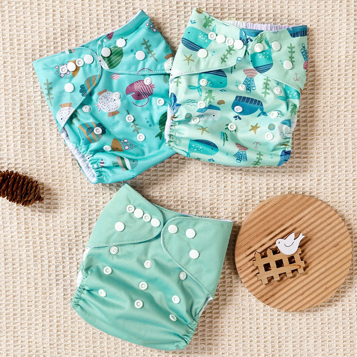 Three reusable cloth baby diapers with ocean fish and whale patterns and one solid teal diaper with snap closures.