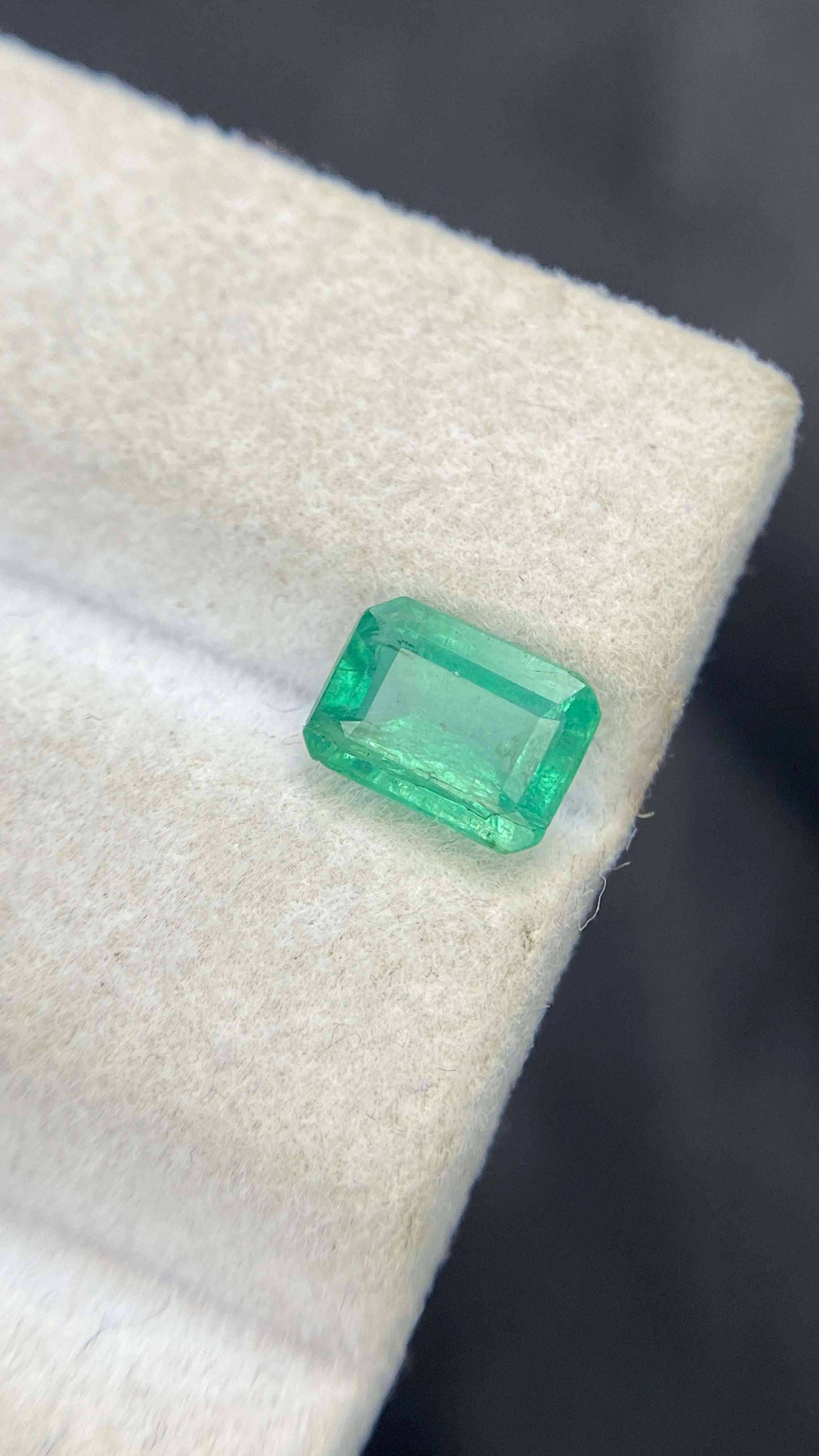 Loose emerald-cut green gemstone, tilted view on white felt pad