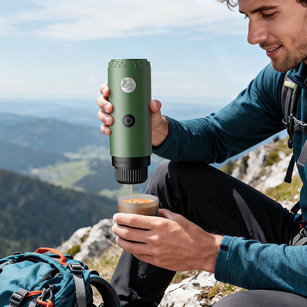 Green portable electric espresso maker for travel, brewing coffee outdoors with a mountain backdrop.