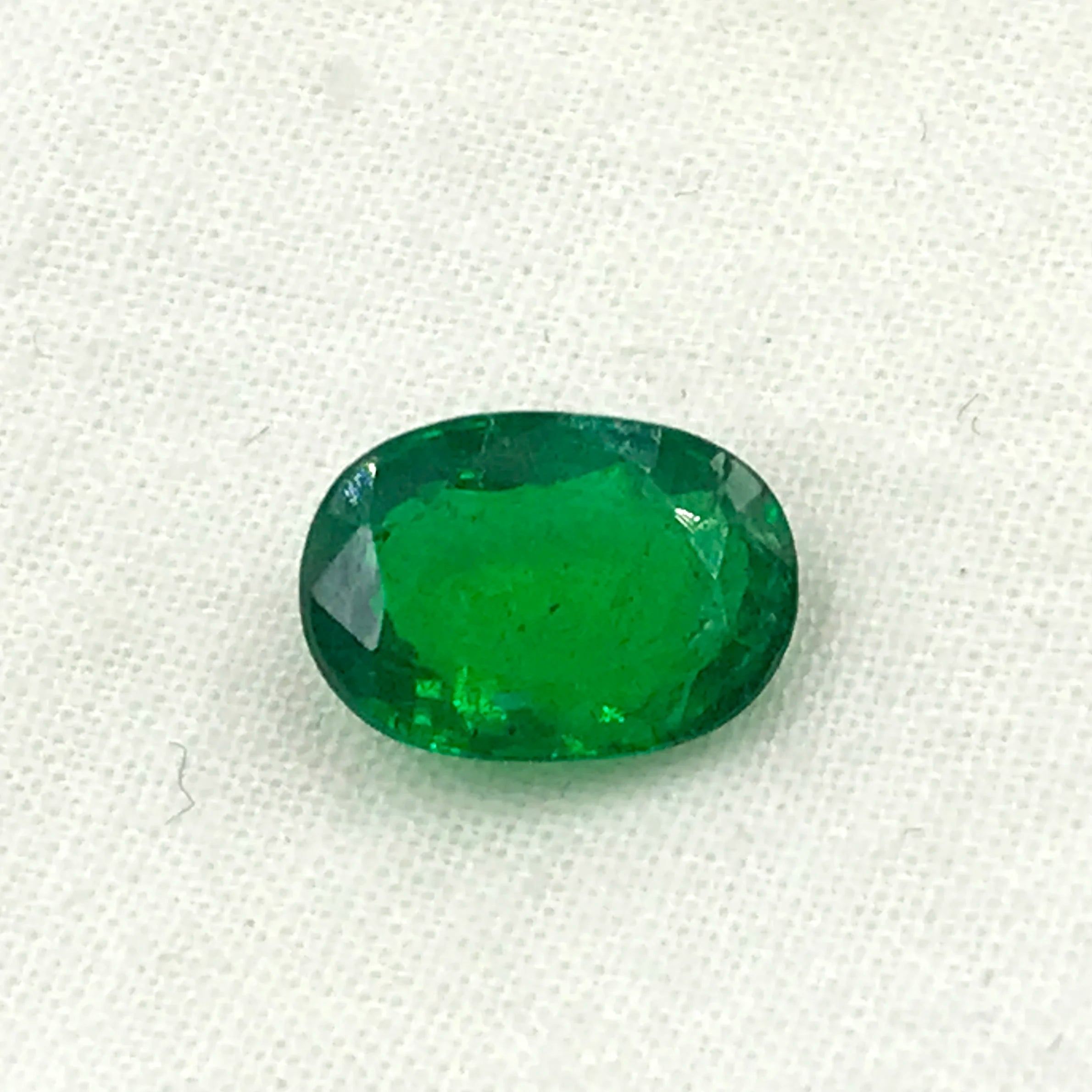Green oval faceted gemstone on white cloth, loose stone