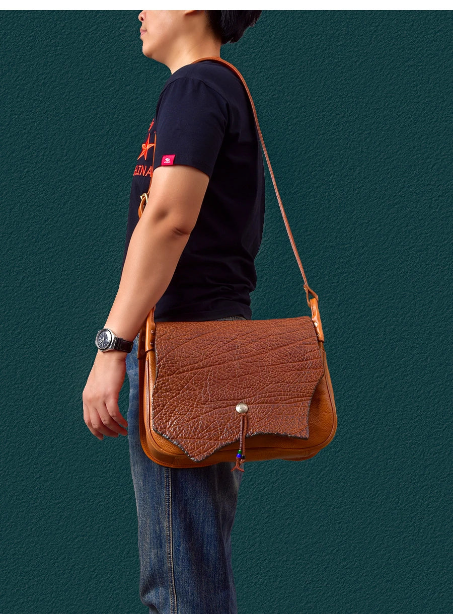 Vintage handmade brown cowhide messenger bag with textured leather flap, metal snap, and adjustable shoulder strap.