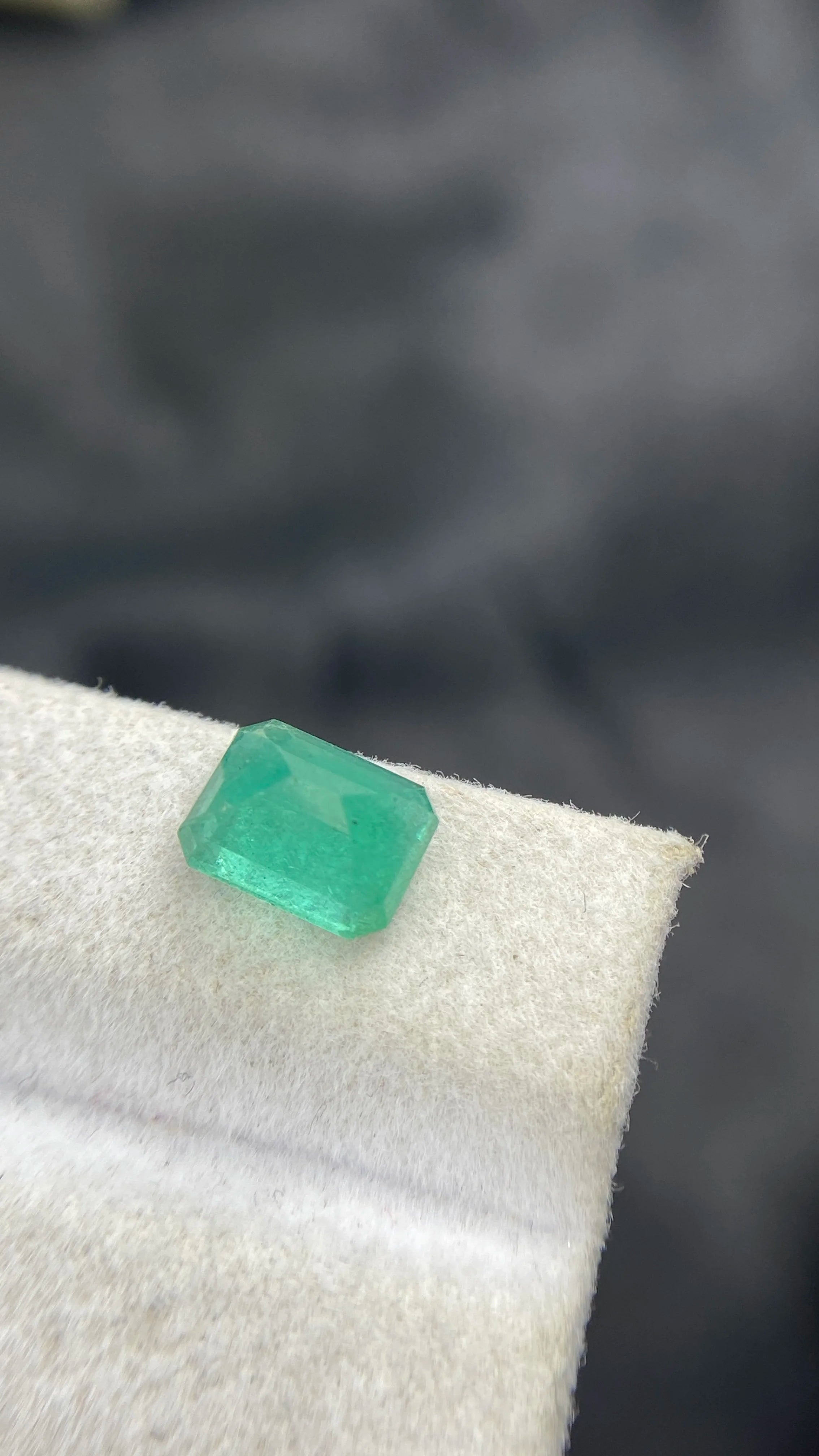 Small emerald-cut green gemstone detail on white felt