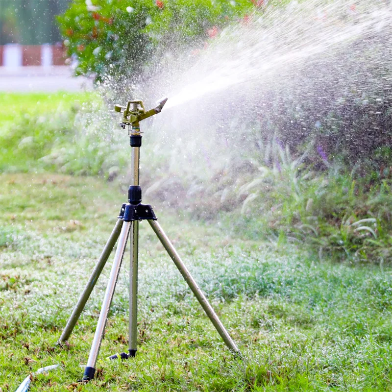 Gold rotating tripod sprinkler with blue base, spraying wide water pattern