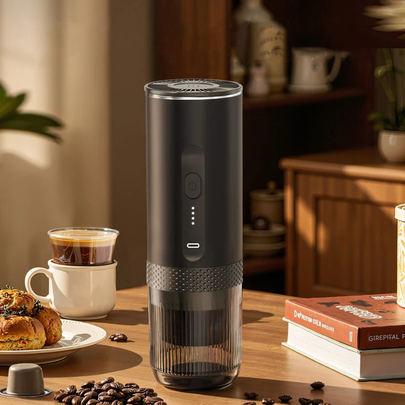 Matte black portable electric coffee maker with transparent base, power button, and status indicator lights on table.