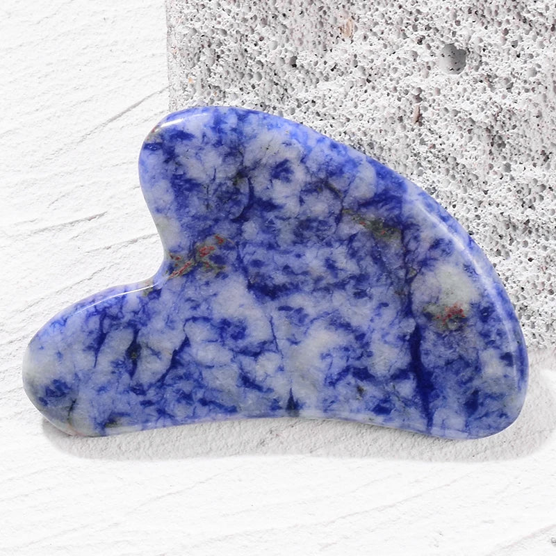 Blue and white marble-patterned heart-shaped gua sha facial massage tool resting on a textured surface.