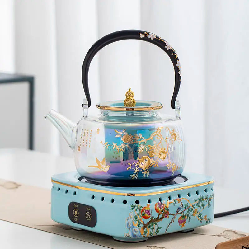 Electric glass tea kettle set with gold floral art on a matching blue ceramic base with heat controls.