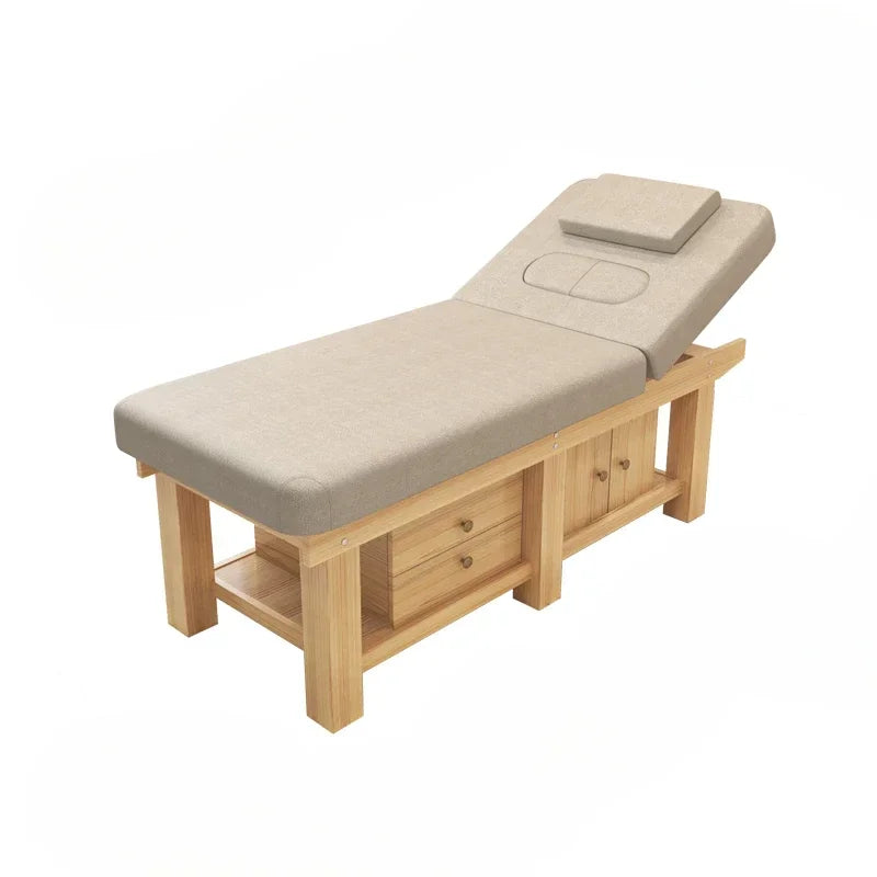 Beige massage table with adjustable headrest, wooden base, drawers, and cabinet, isolated on a white background.