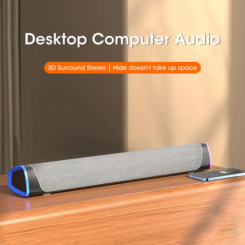 Computer speaker bar on desk with gray grille, blue end lights, and phone beside it
