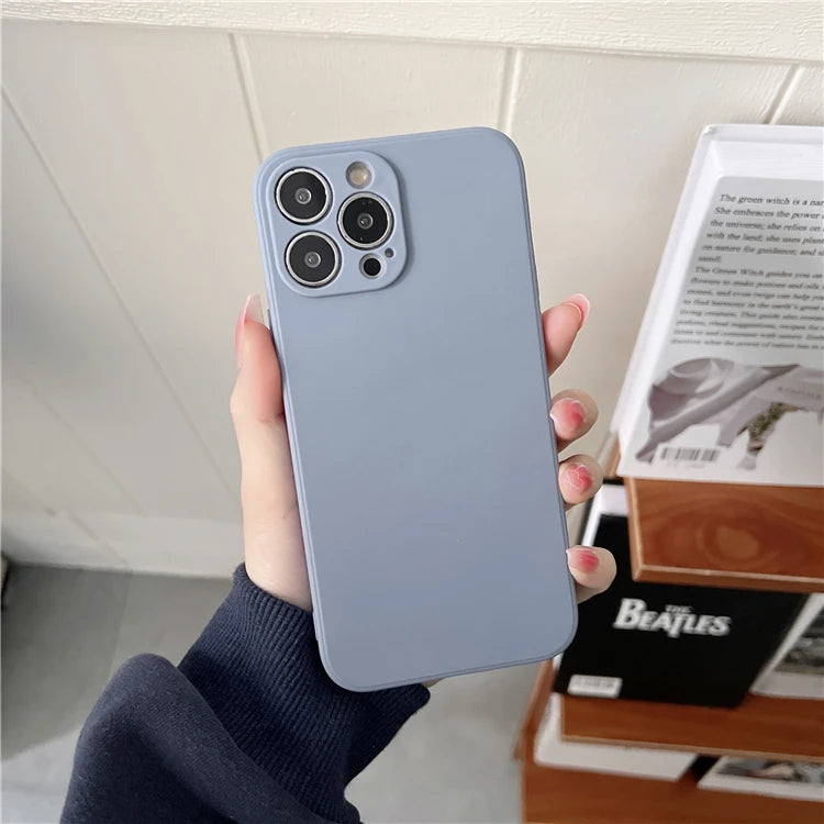 Matte, periwinkle blue silicone iPhone case with a square camera cutout held in a hand.