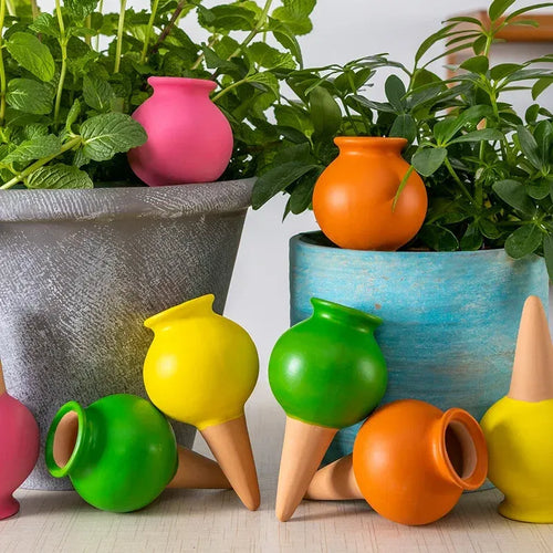 Assorted ceramic watering droppers with cone nozzles beside potted green plants