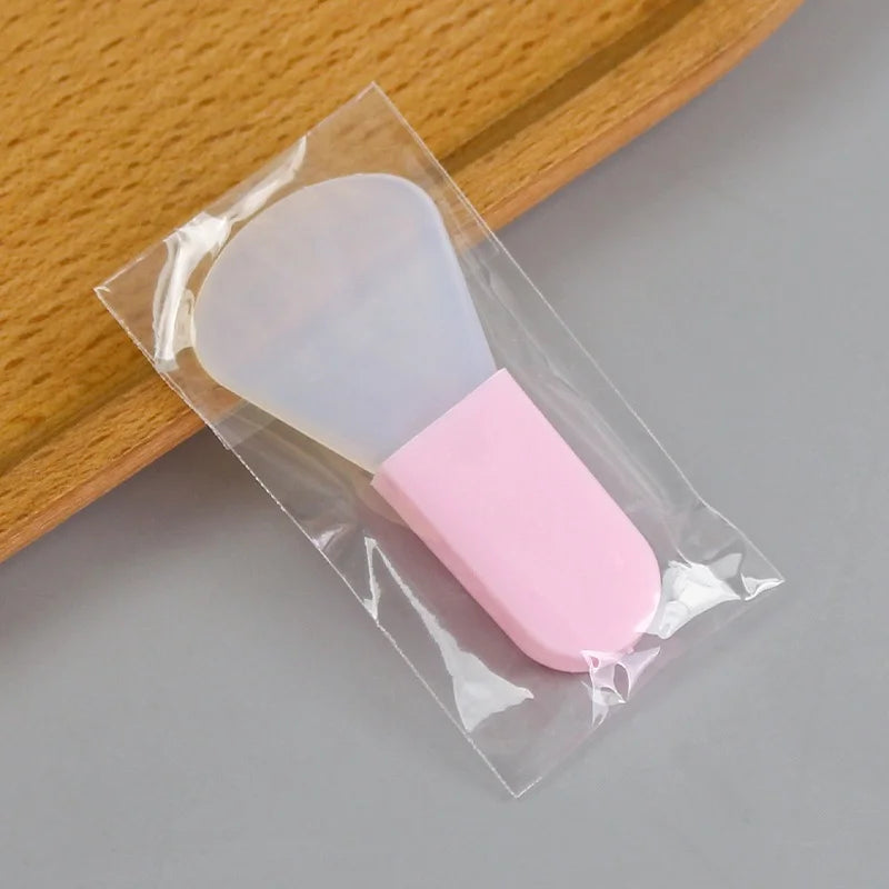 Silicone facial mask brush with a translucent head and pink handle, packaged in a clear plastic sleeve.