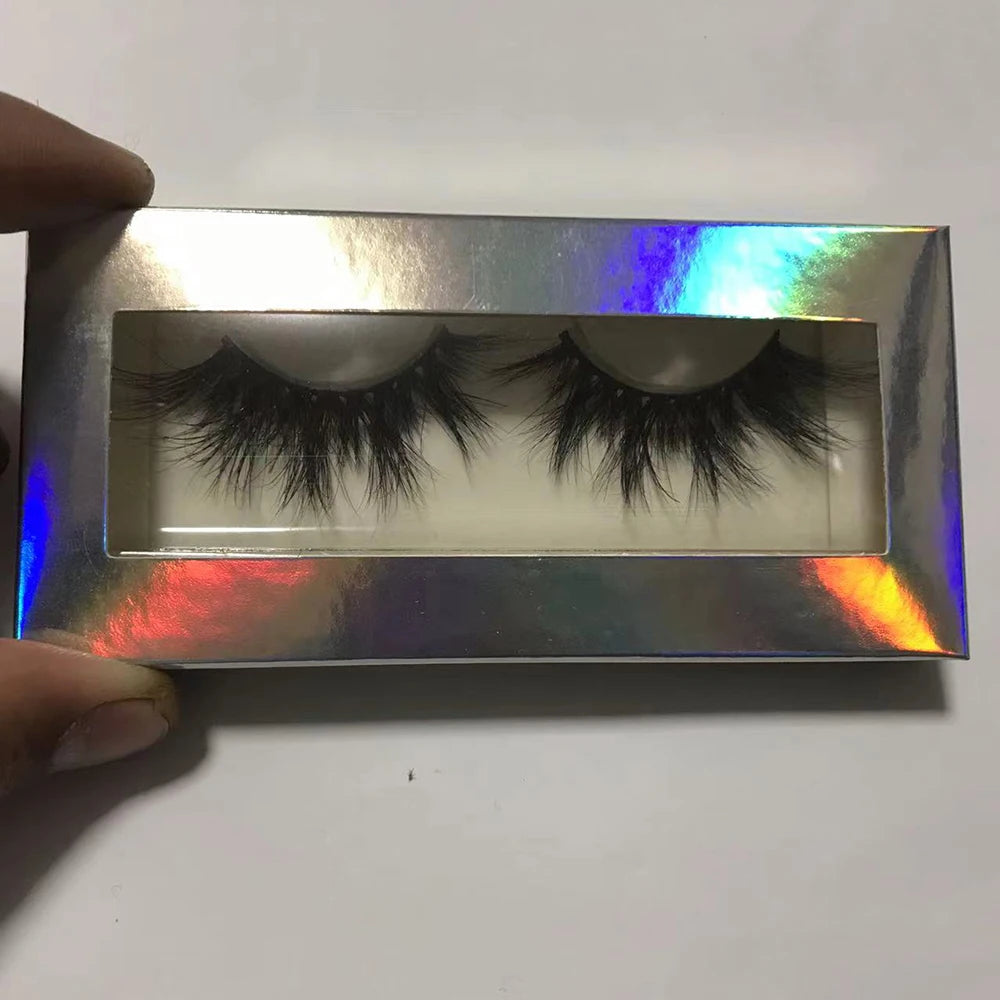 Pair of 3D black mink false eyelashes in a rectangular, holographic silver box held by a hand.