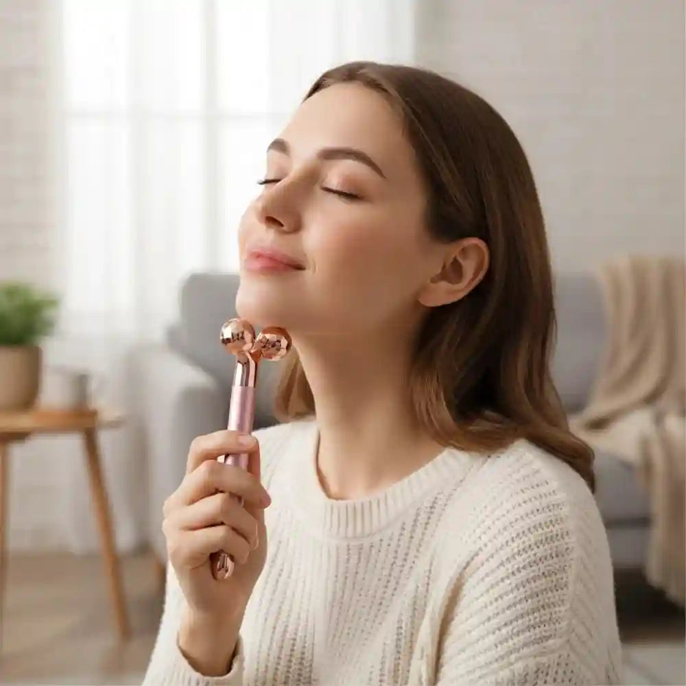 A woman uses a rose-gold, dual-ball facial massager on her jawline.