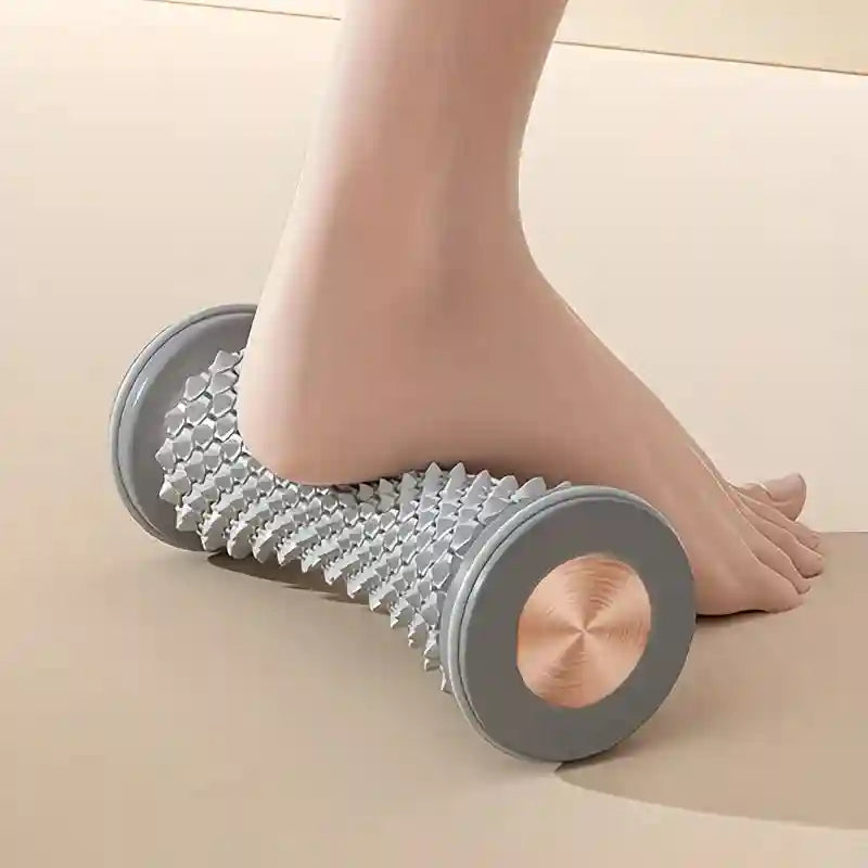 Grey spiked plantar fascia massage roller tool under foot for muscle relaxation and home fitness therapy.