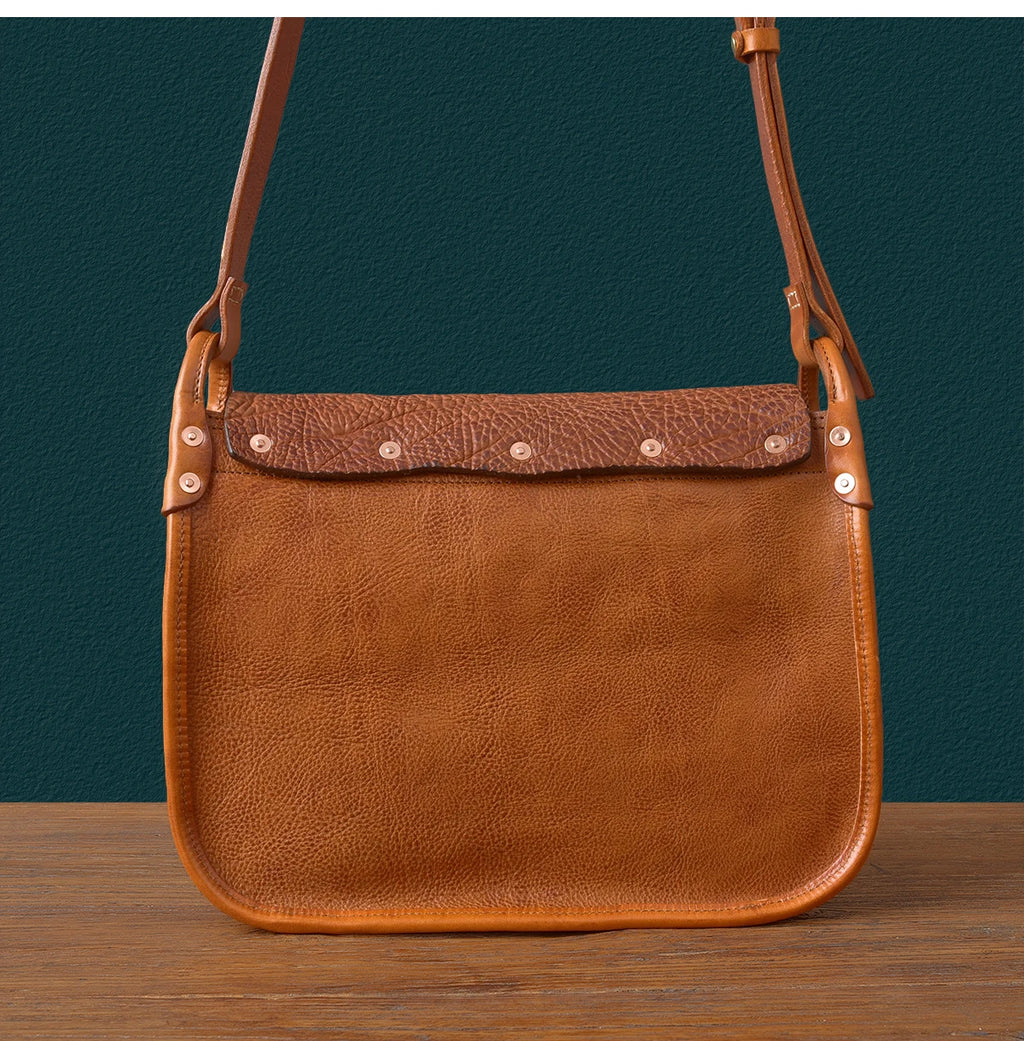 Tan genuine cowhide messenger bag with textured flap, rivet details, and adjustable shoulder strap. Vintage luxury style.