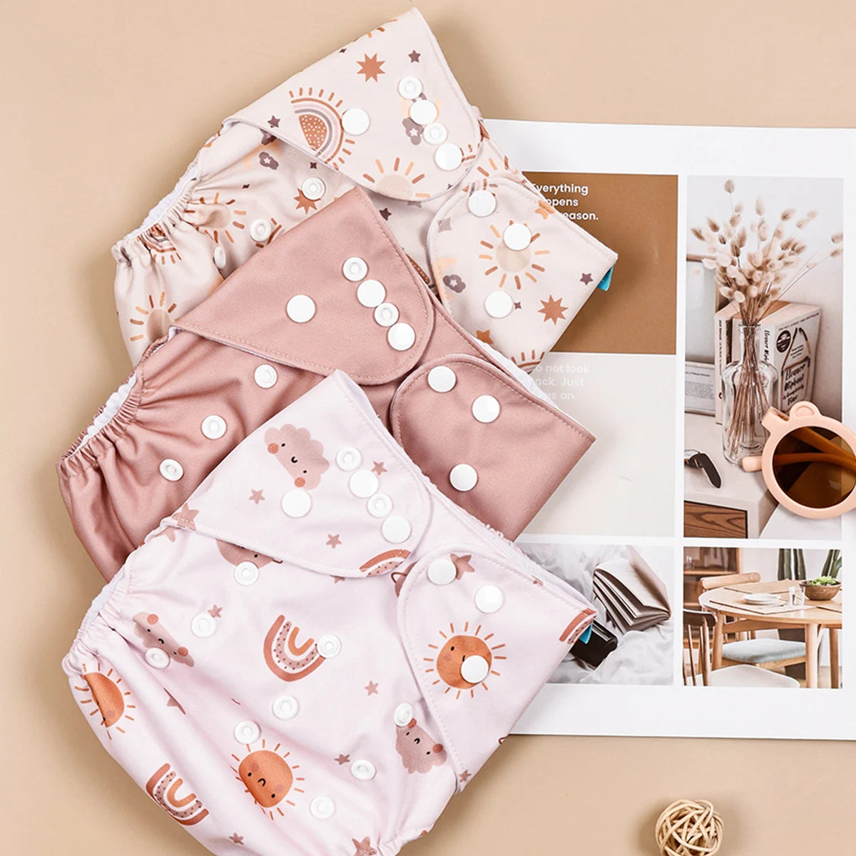 Reusable cloth diapers with boho sun, rainbow, and cloud patterns in pink and beige tones. Adjustable baby care gear.