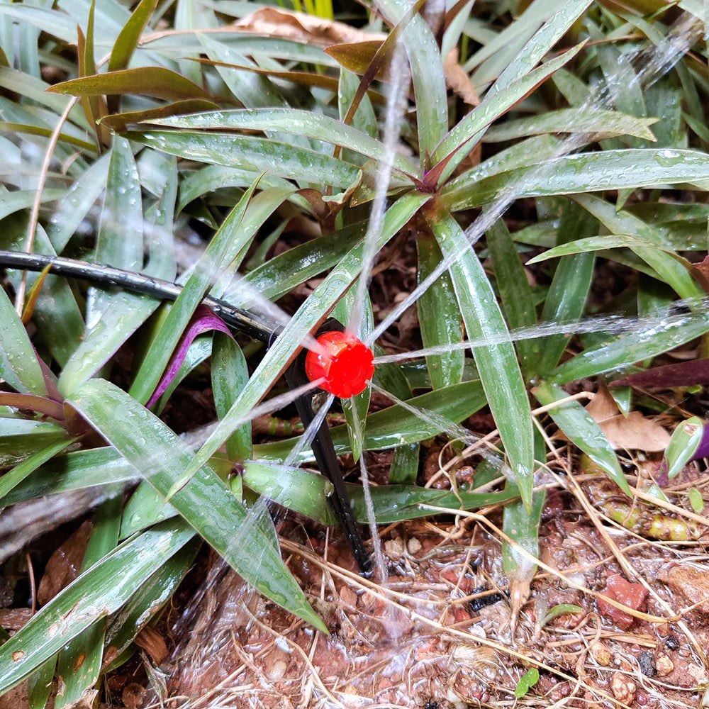 Red 8-hole drip emitter spraying water into garden soil among grass and leaves