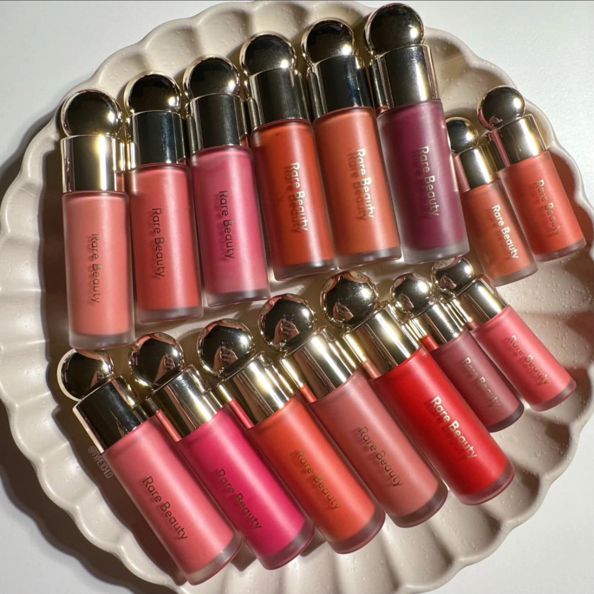 Rare Beauty waterproof liquid blush and lipstick collection in various matte shades on a decorative white dish.