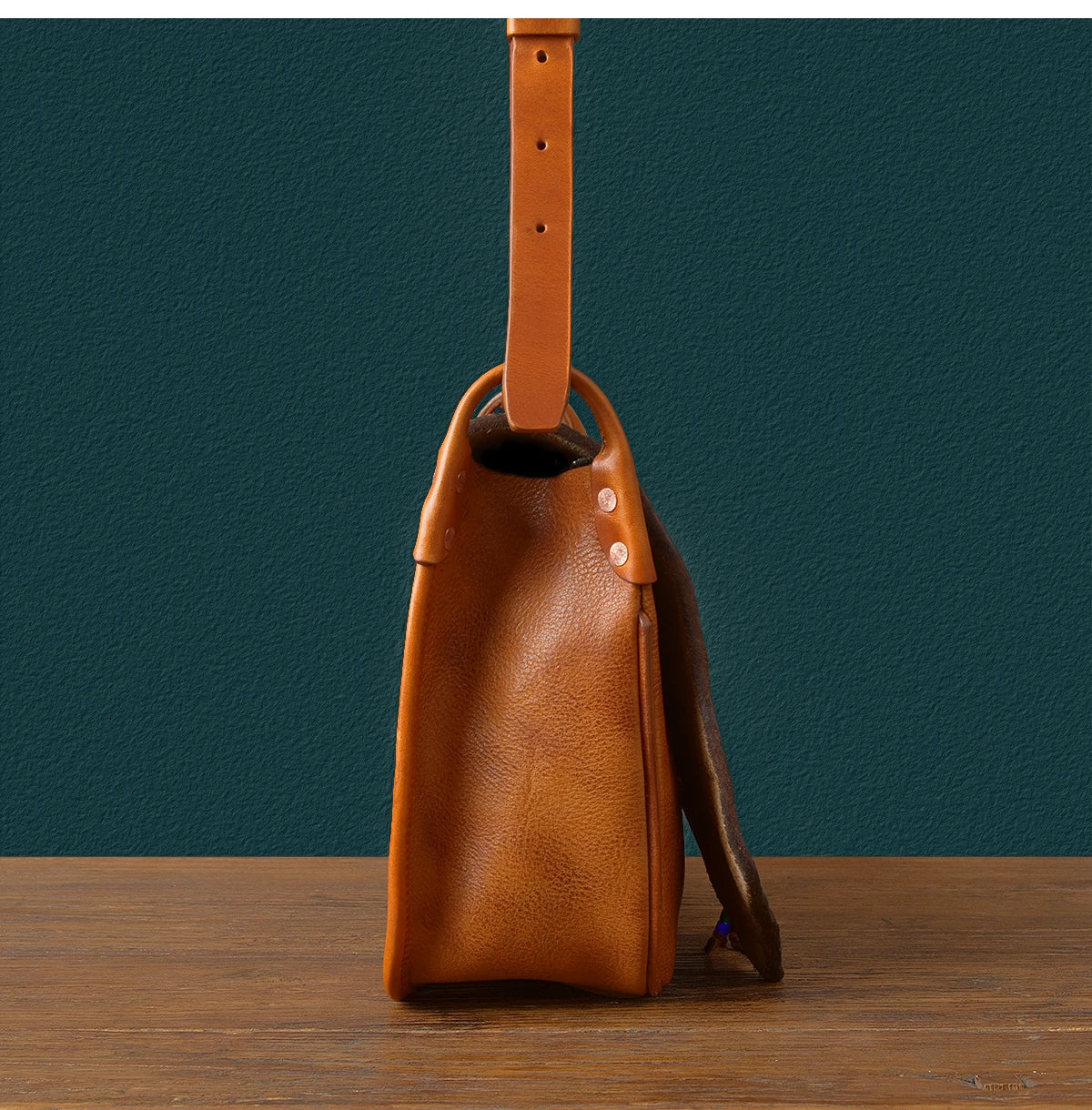 Vintage handmade tan cowhide leather messenger bag with adjustable strap, side view showing premium grain detail.