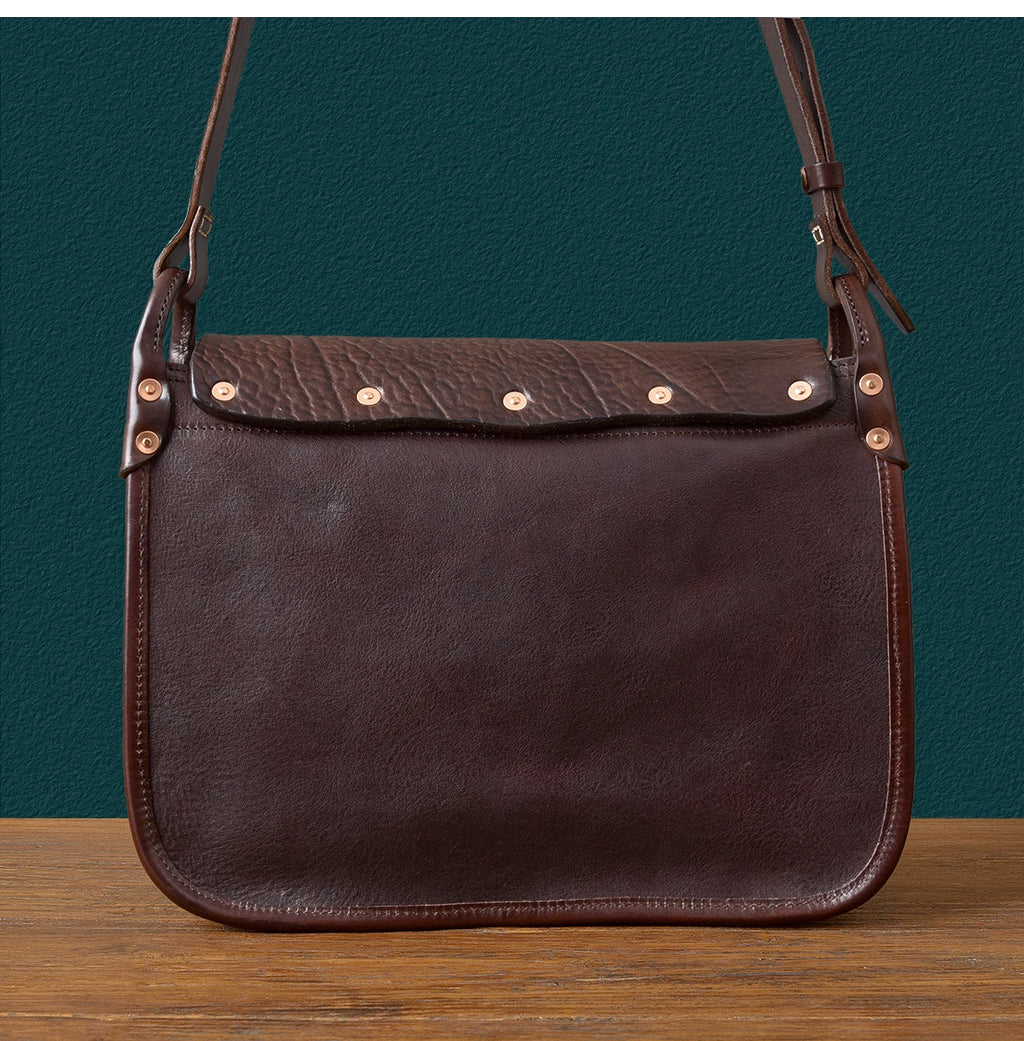 Vintage dark brown genuine cowhide messenger bag with rivet detailing, adjustable shoulder strap, and luxury design.