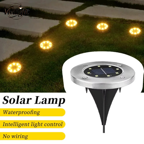 Round silver solar disk light with a black ground spike, illuminating a grassy garden path.