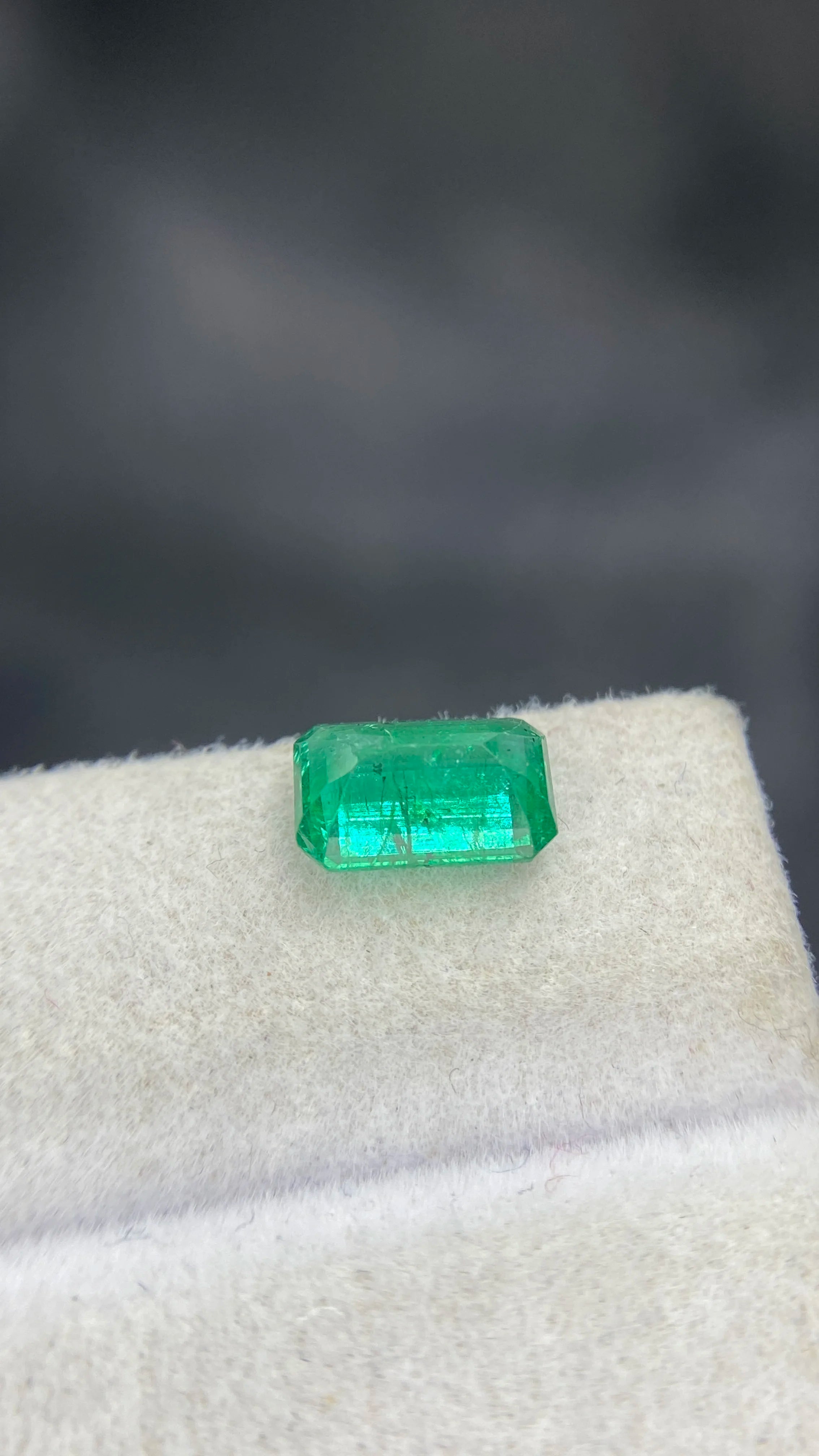 Green emerald-cut gemstone, loose faceted stone shown on white padding