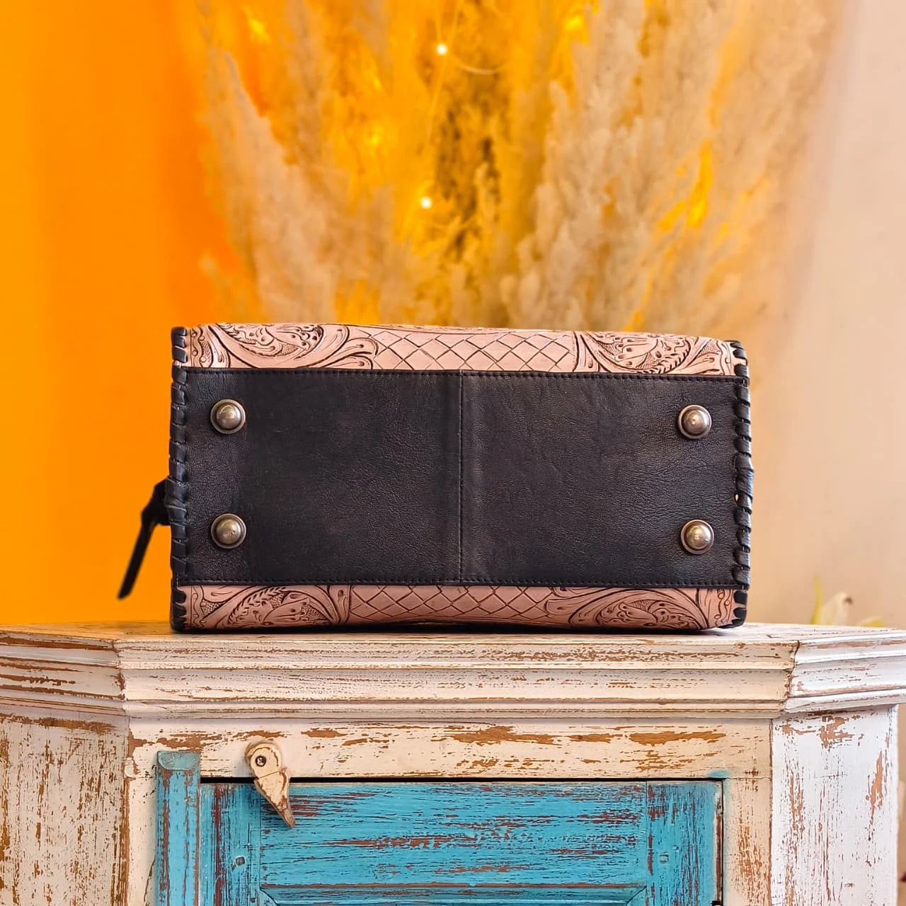 Luxury hand-tooled floral leather weekender trunk bag with black base, contrast stitching, and metal protective feet.