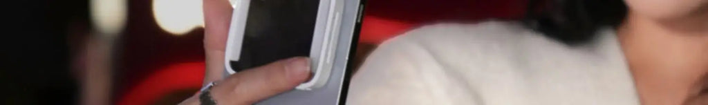 A white magnetic phone grip attached to the back of a black smartphone held in hand.