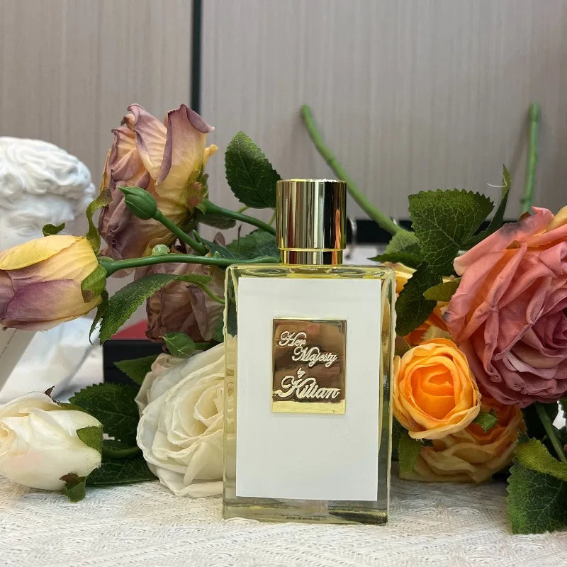 Her Majesty perfume in a clear glass bottle with a white label and gold cap, surrounded by artificial roses.
