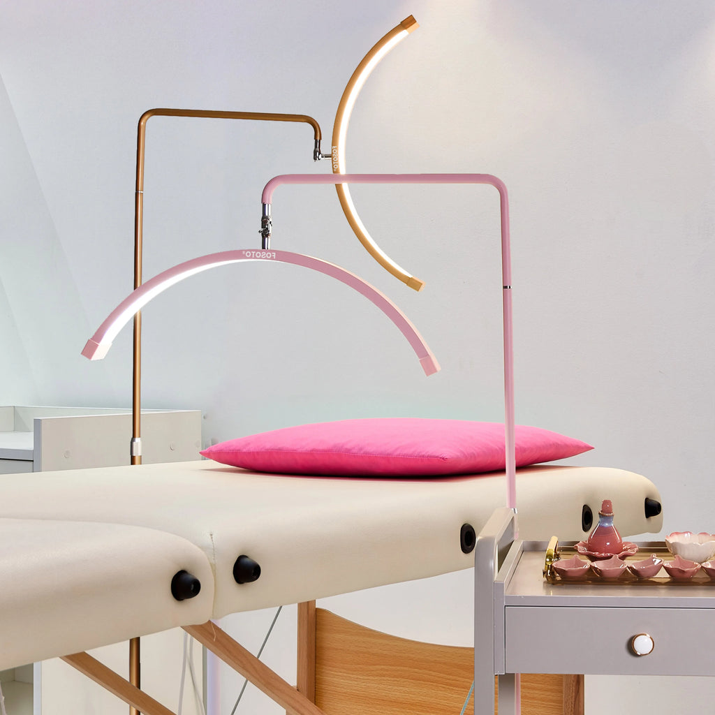 Crescent-shaped LED floor lamps in pink and gold, used for professional beauty treatments over a treatment table.