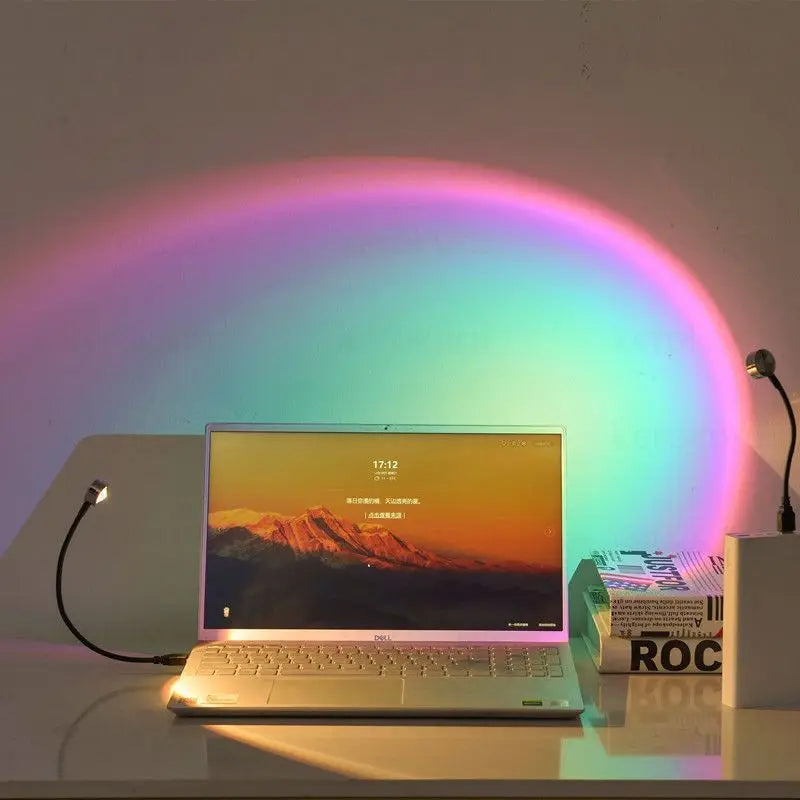 USB sunset lamp with a flexible black neck, projecting a vibrant rainbow arc on the wall behind a laptop.