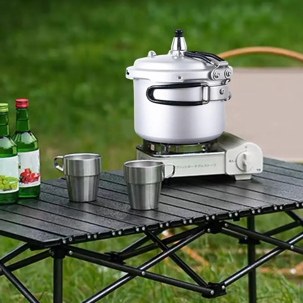 Portable pressure cooker on a folding camp stove with two metal cups nearby