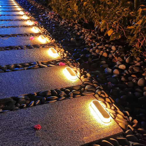 Warm white solar deck step lights glowing along a garden walkway edge, 4-pack.