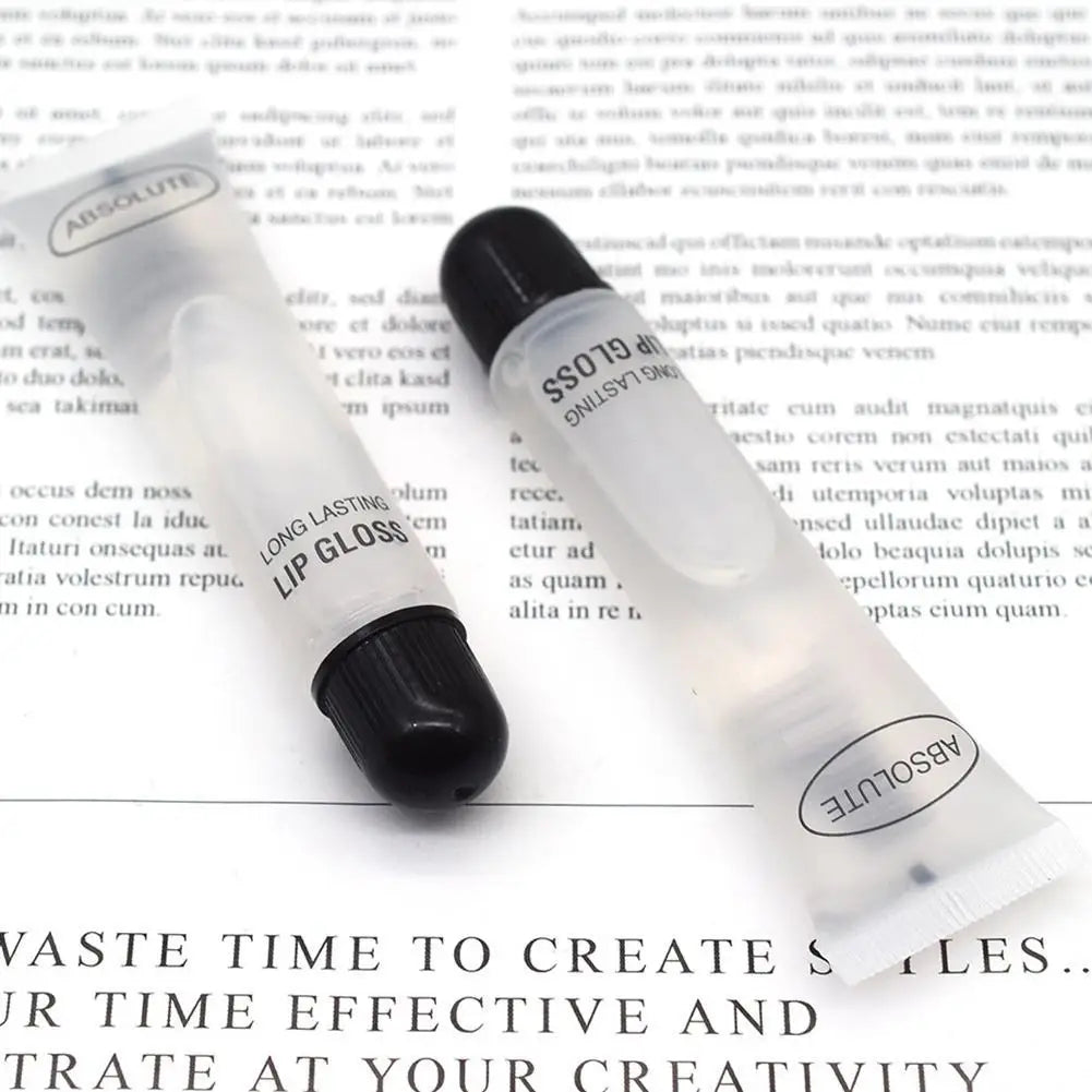 Two transparent, long-lasting lip gloss tubes with black caps on a paper background. Hydrating and smoothing lip makeup.