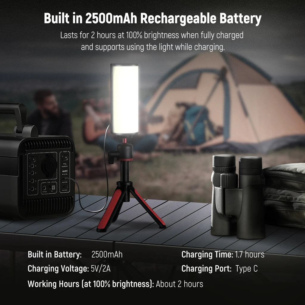 Cylindrical LED video light on a small black and red tripod, charging from a power station at a campsite.