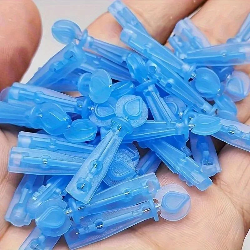 A handful of small, blue translucent plastic disposable lancet needles for acne and blackhead removal.