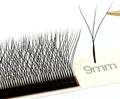 Black 3D W-shaped lash extension cluster being held by tweezers, with a strip of identical 9mm lashes on a tray.