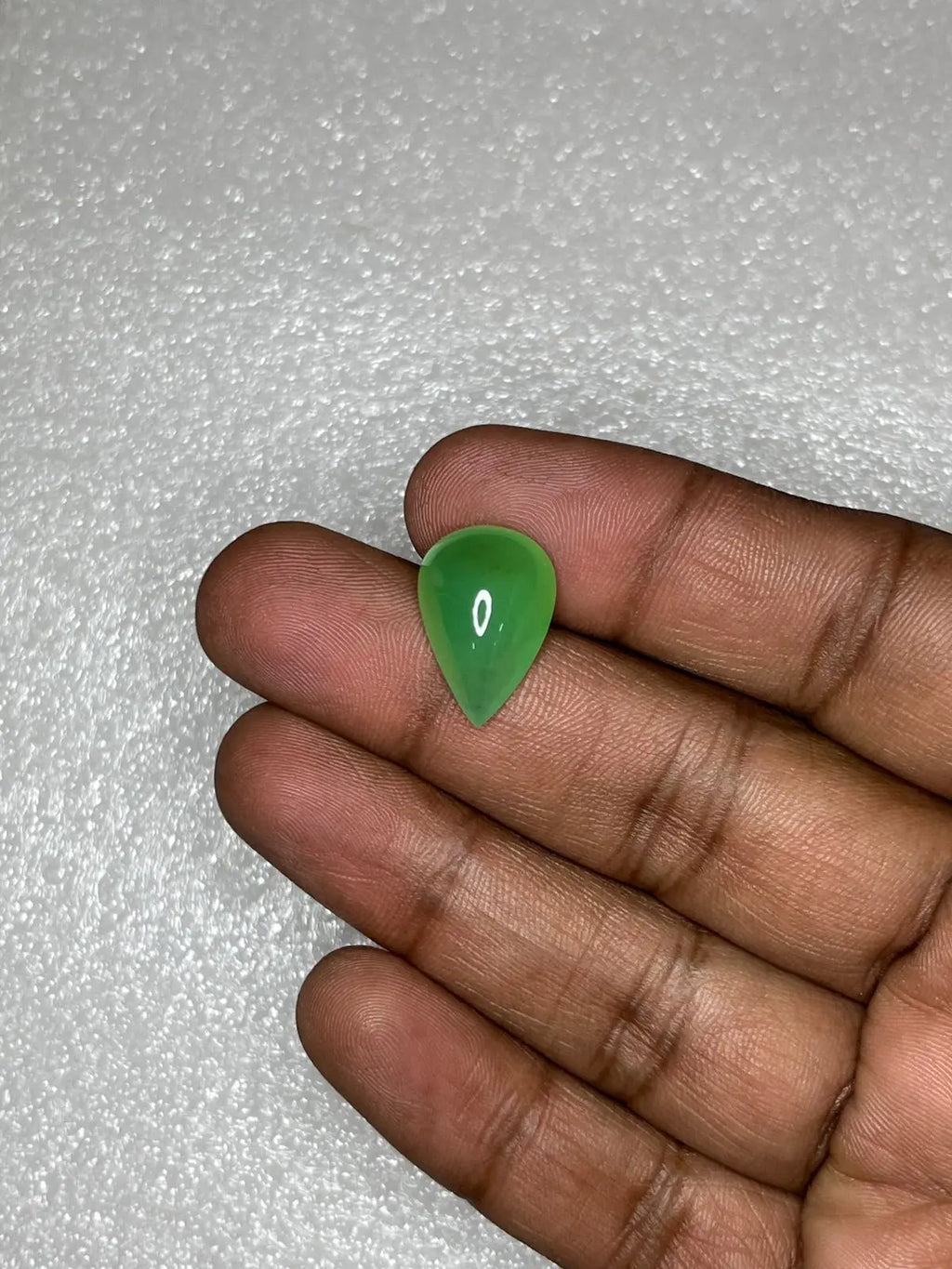 Green chrysoprase pear-shaped cabochon gemstone in fingers, polished teardrop with highlight.